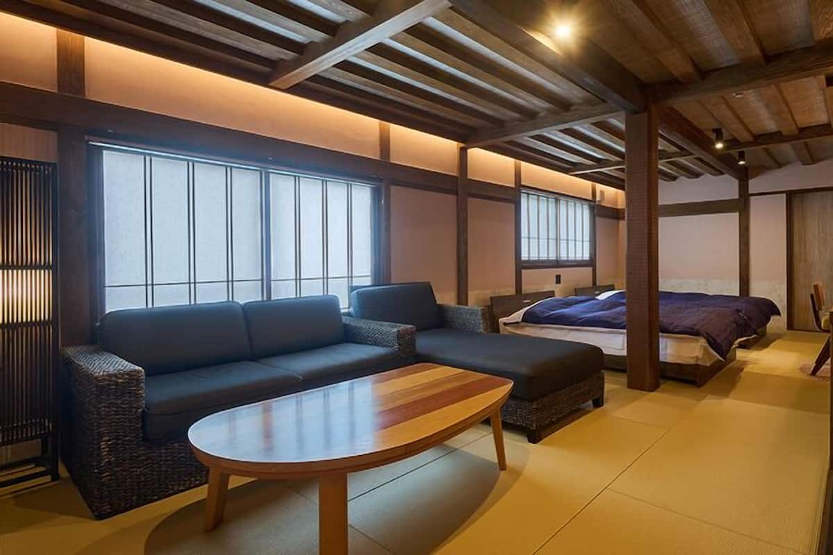 A traditional Japanese-style room with tatami flooring, a low wooden ceiling, a sofa, a bed, and a small table.