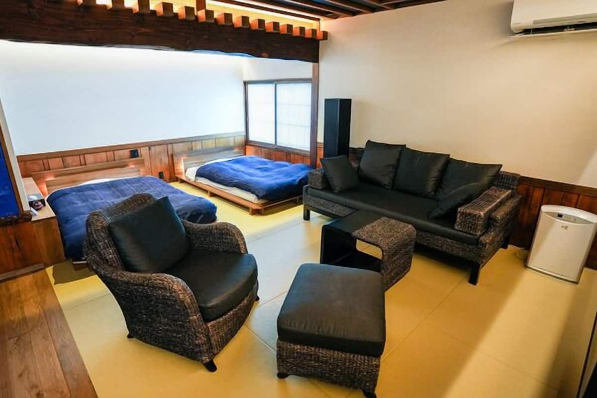 A room with a bed, a sofa, a chair, a small table, and an air conditioning unit.
