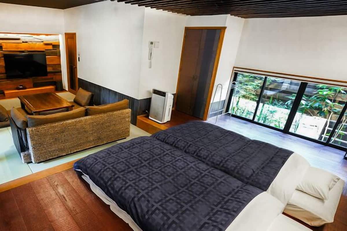 A bedroom with a large bed, a sofa, a TV, and a view of greenery.
