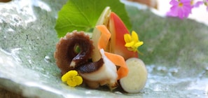 A dish with seafood, vegetables, and flowers on a textured plate.