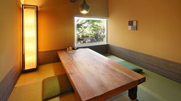 Una habitación tradicional japonesa con suelo de tatami, una mesa de madera baja y vista a la vegetación a través de una ventana.