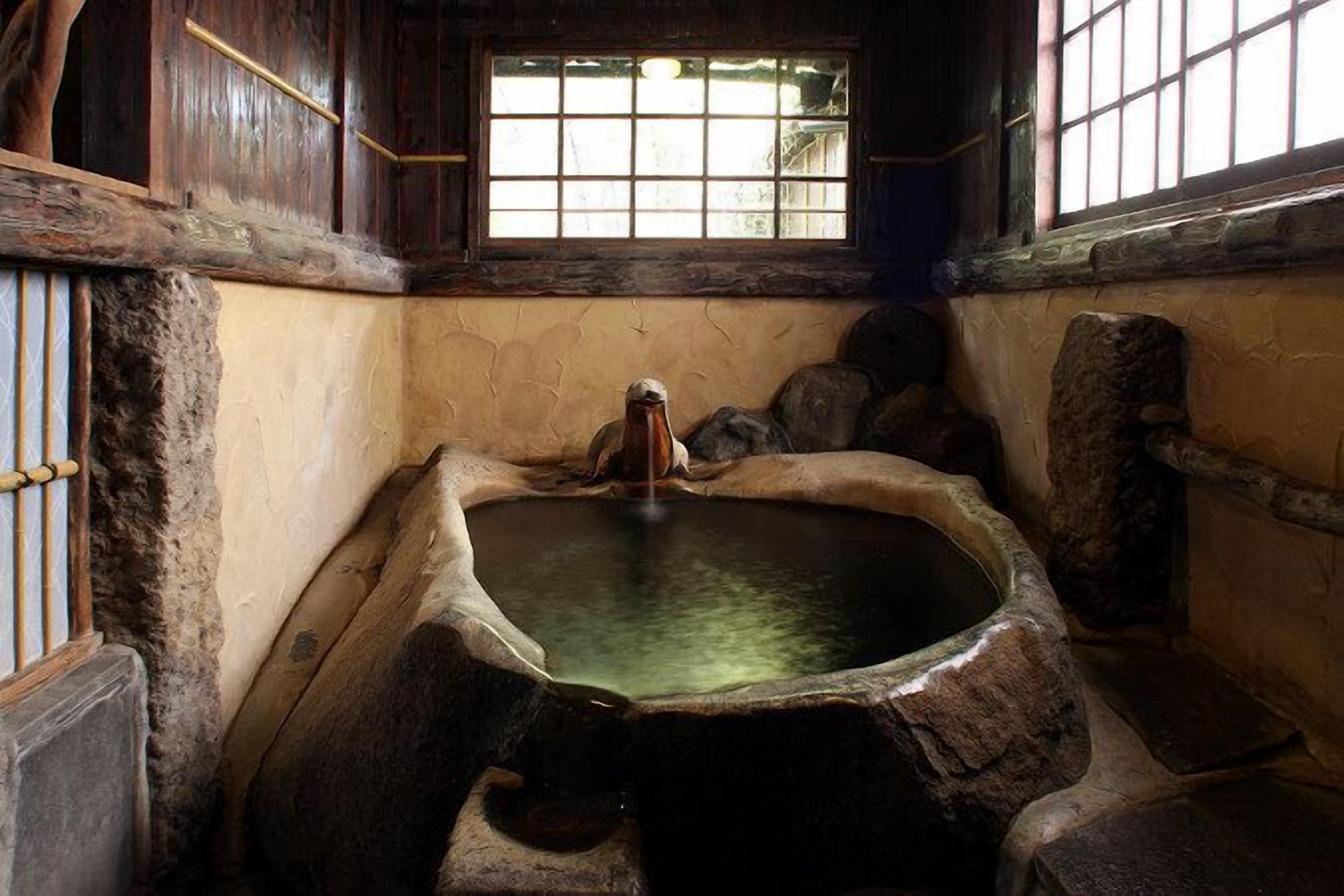 A stone hot spring bath with a wooden bench, a window with bars, and a stone wall.