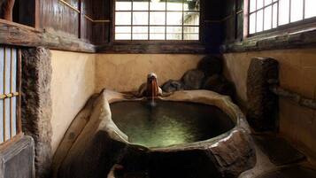 A stone hot spring bath with a wooden bench, a window with bars, and a stone wall.