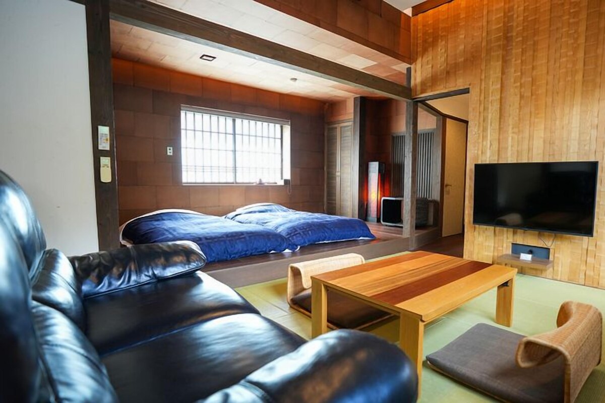 Ein modernes Wohnzimmer mit einer Ledersofa, einem Holztisch und einem an einer Holzwand befestigten Fernseher.