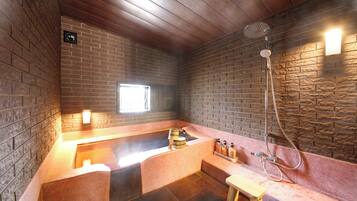 A stone-walled room with a wooden ceiling, a built-in bathtub, and a shower area.