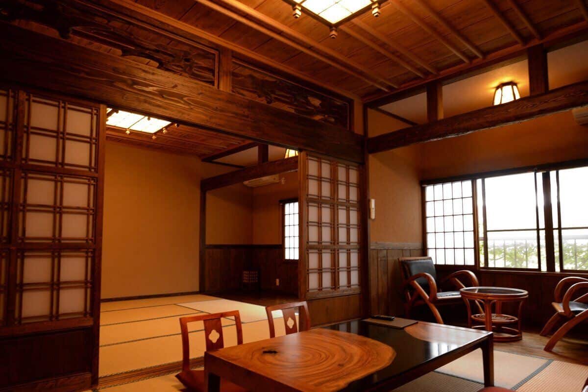 A traditional Japanese room with tatami flooring, wooden furniture, sliding doors, and large windows.