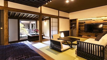 Una habitación tradicional japonesa con suelo de tatami, una mesa baja, un sofá y un televisor.