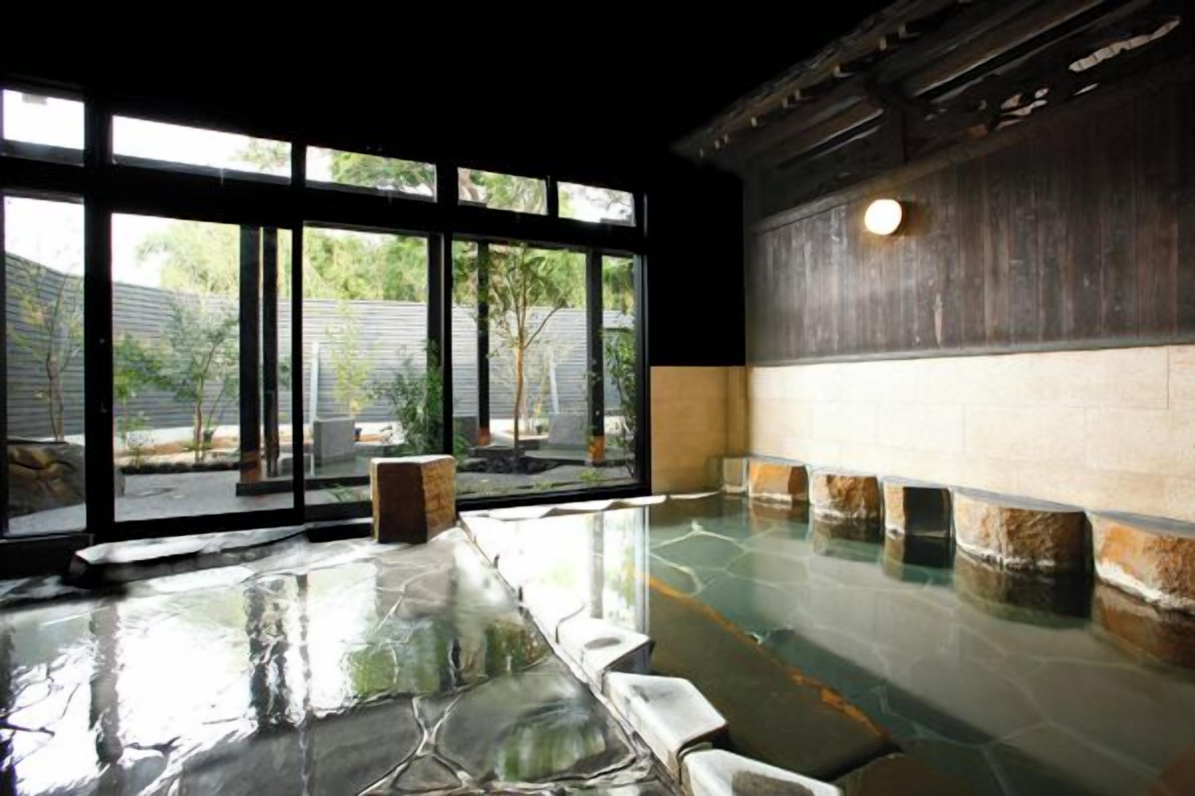 A room with a stone floor, large windows, and a view of greenery outside.