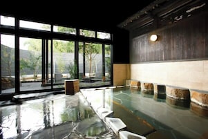 A room with a stone floor, large windows, and a view of greenery outside.