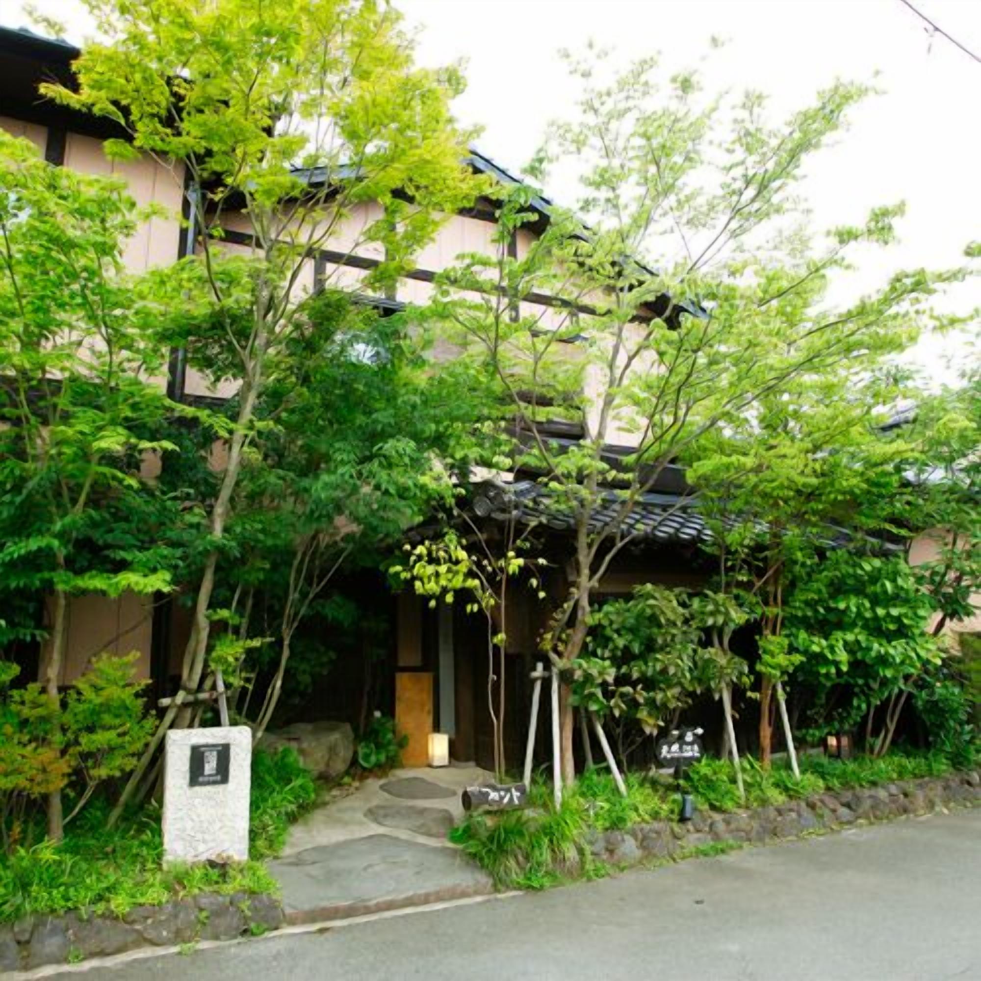 A traditional Japanese building with a stone pathway leading to the entrance, surrounded by lush greenery.