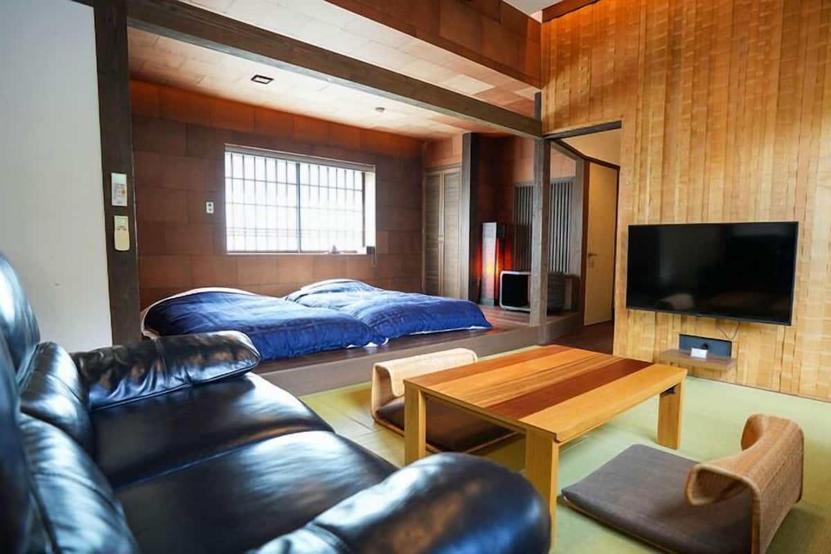 A modern living room with a leather sofa, a wooden coffee table, and a TV mounted on a wooden wall.