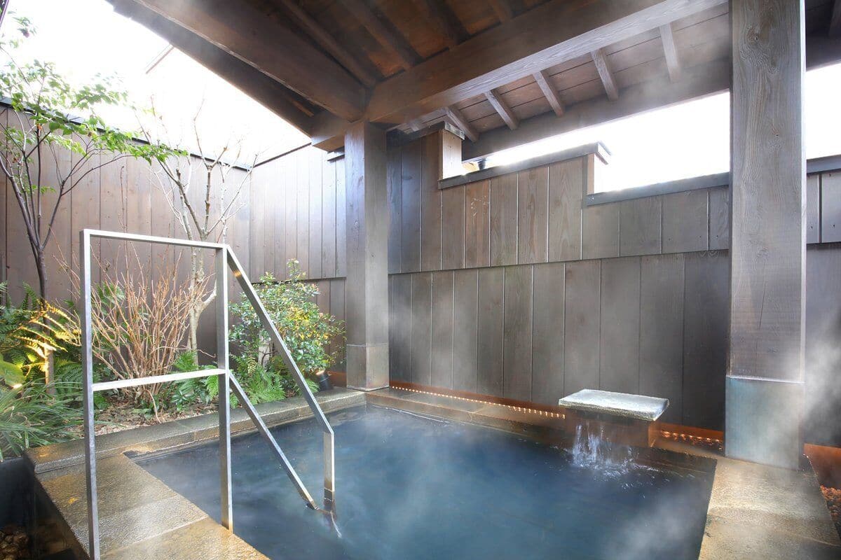 A hot spring with a metal ladder, surrounded by wooden walls and plants.