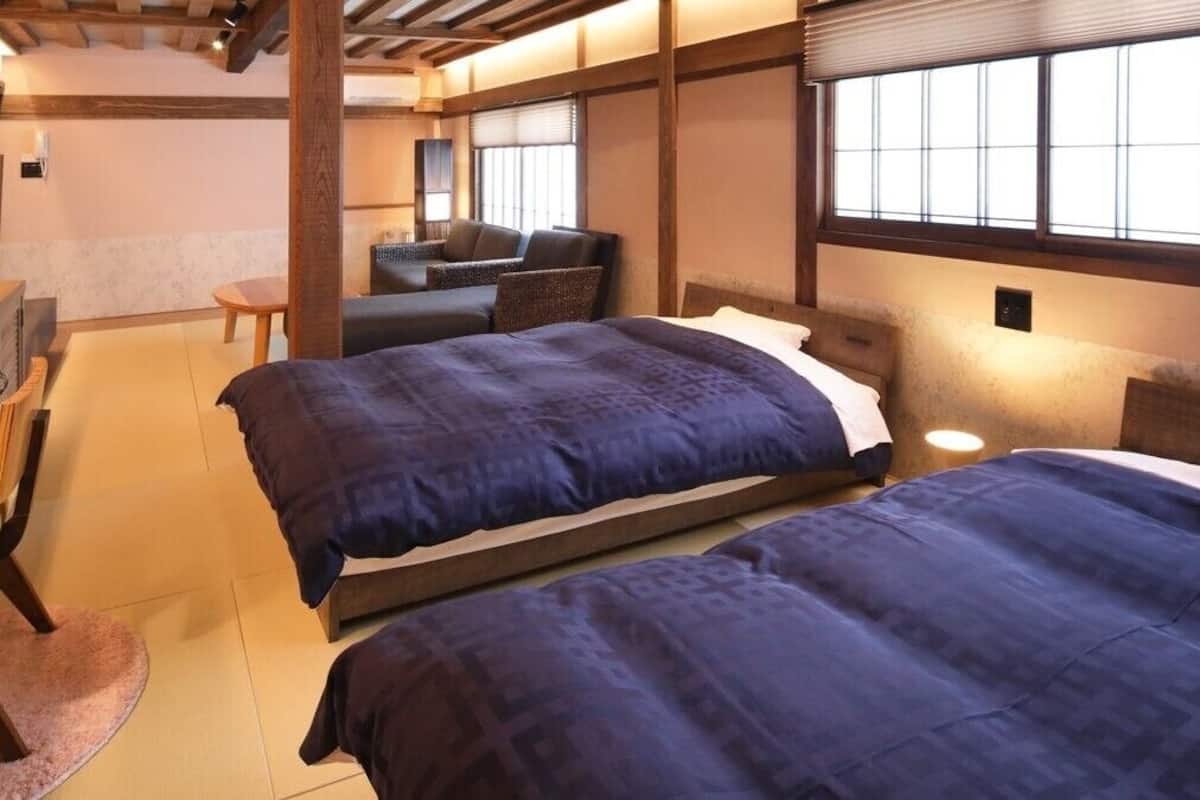 A traditional Japanese-style room with tatami flooring, a low wooden desk, two beds with dark bedding, and a sliding shoji screen window.