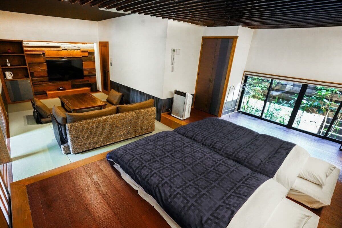 A modern bedroom with a large bed, a sofa, a television, and a sliding door leading to a balcony.