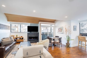 A modern living room with a fireplace, a sofa, a dining area, and a TV mounted on the wall.