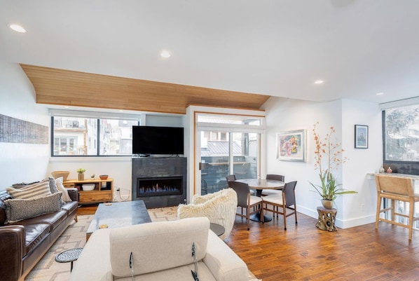 A modern living room with a fireplace, a sofa, a dining area, and a TV mounted on the wall.