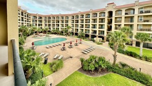 Une cour d’hôtel avec une piscine, des chaises longues et des palmiers.