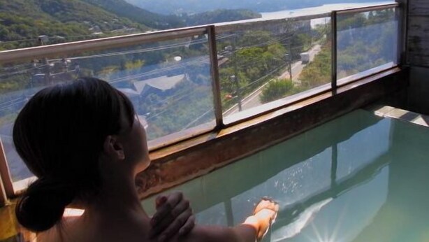 Una persona en una habitación con piso de vidrio, mirando un paisaje con colinas y un río.