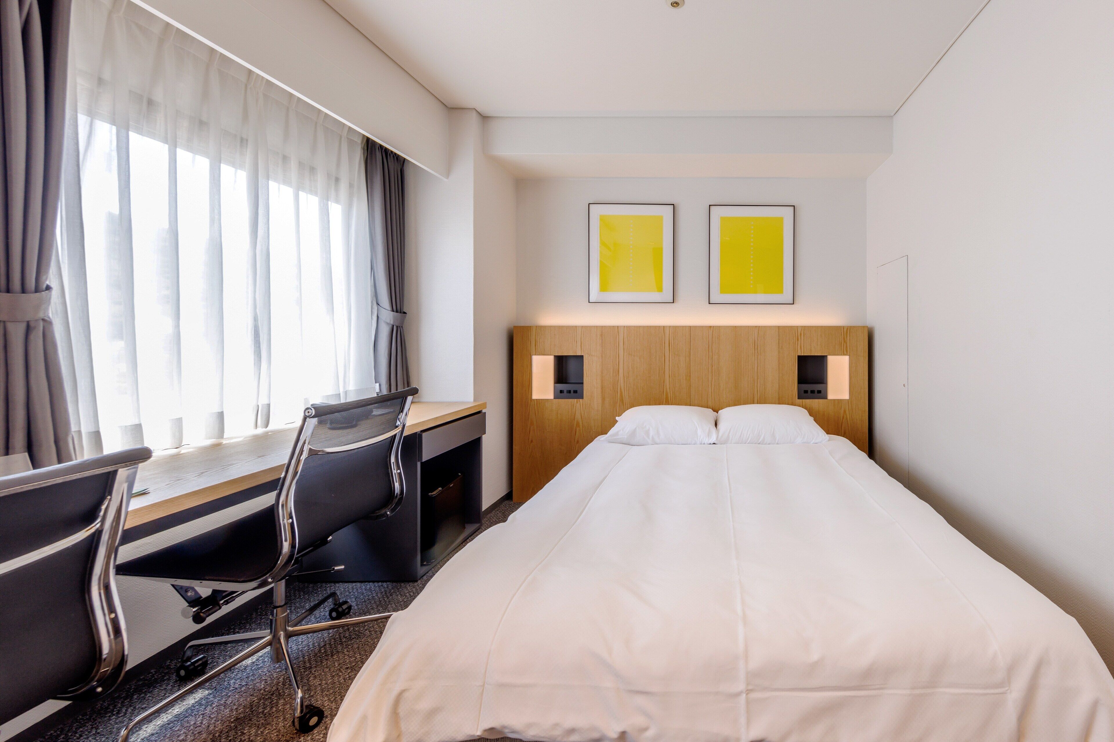 Een hotelkamer met een bed, bureau, stoel en twee foto's in lijsten aan de muur.