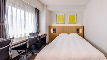 Een hotelkamer met een bed, bureau, stoel en twee foto's in lijsten aan de muur.