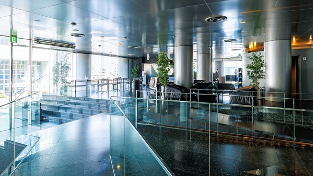 A modern lobby with glass railings, a staircase, and seating areas. - The Grand Palace (Tokushima)
