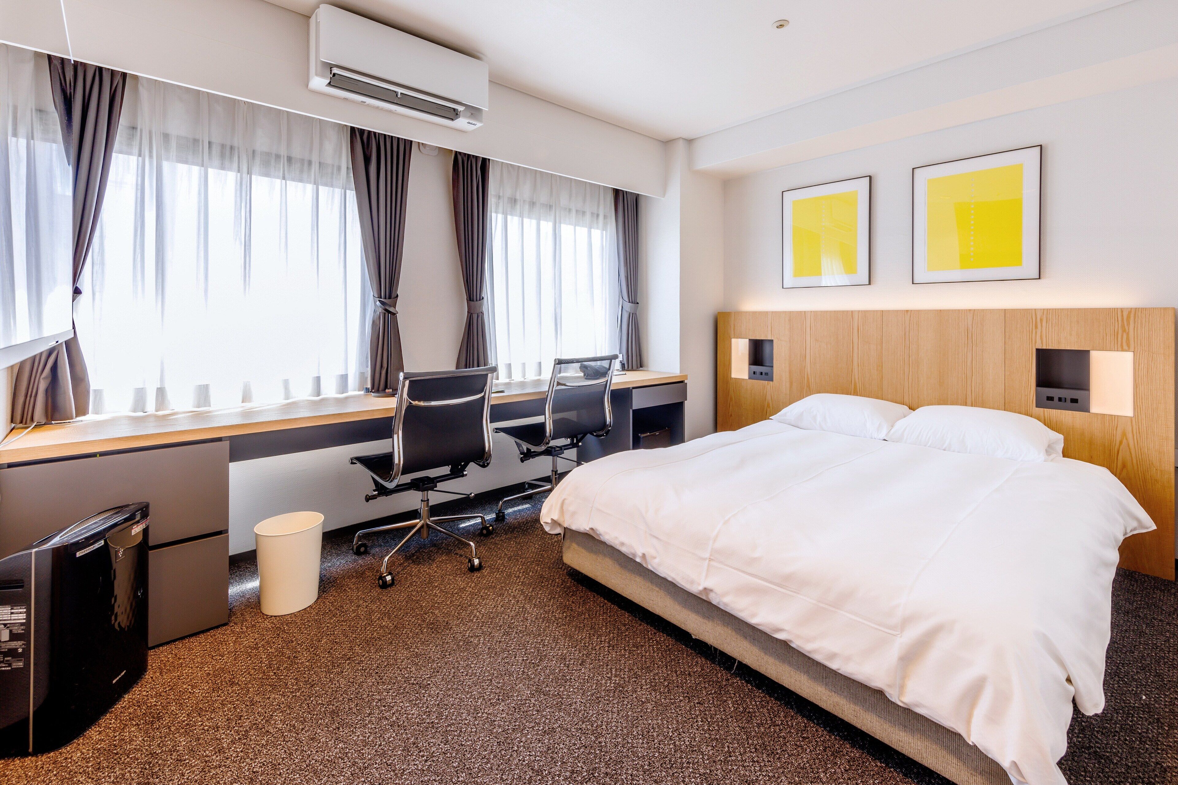 Ett hotellrum med en säng, ett skrivbord, en stol och en luftkonditioneringsanläggning.