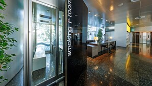 A modern hotel lobby with a glass door labeled "smoking room," a reception desk, and a seating area with chairs and a table. - The Grand Palace (Tokushima)