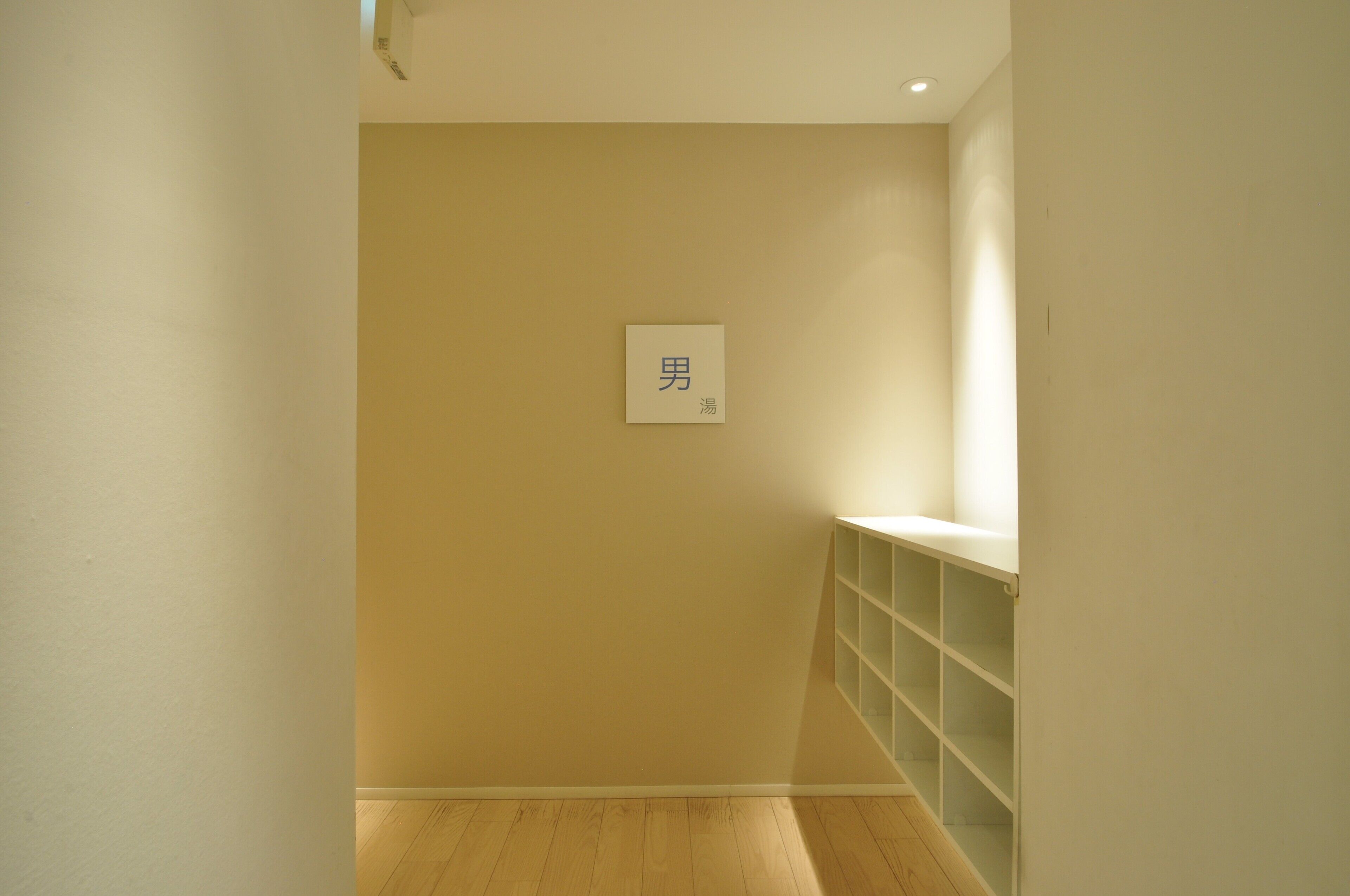 A hallway with a beige wall, a white shelf unit, and a small sign with Chinese characters.