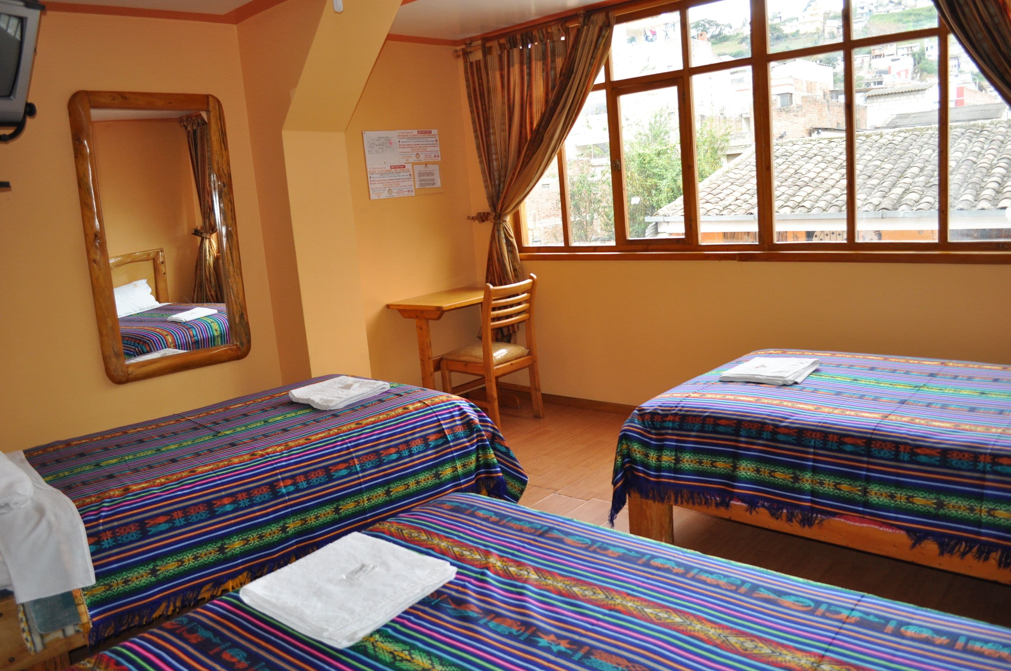 A room with two beds, a wooden desk, a chair, a mirror, and a window with curtains.