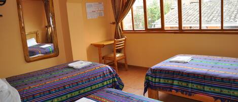 A room with two beds, a wooden desk, a chair, a mirror, and a window with curtains.