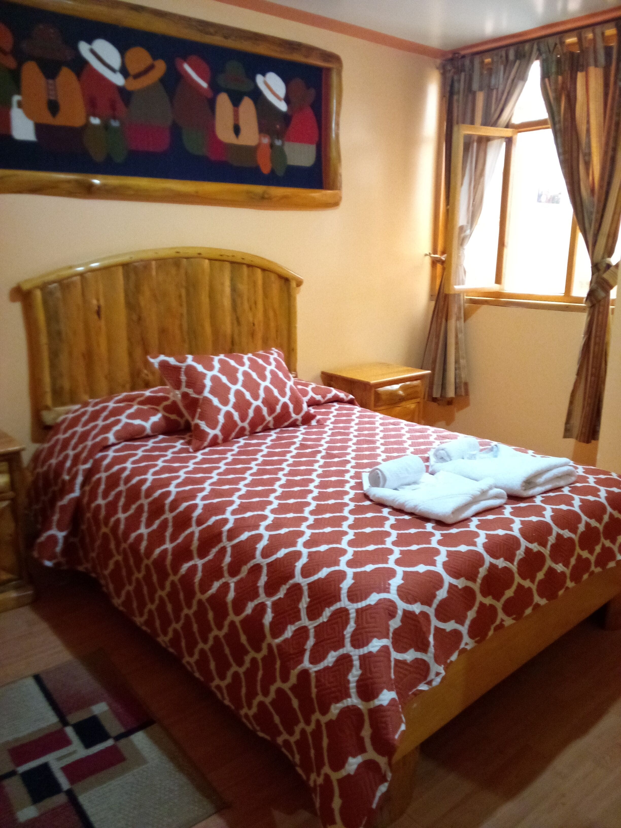 A bed with a red and white patterned bedspread, a wooden headboard, and a nightstand with a lamp.