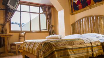 Una habitación con cama, una silla, una mesa, un ventanal y un cuadro en la pared.