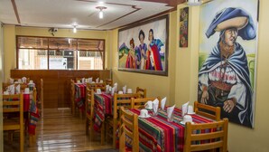 Un restaurante con mesas y sillas de madera, manteles de colores y cuadros en las paredes.