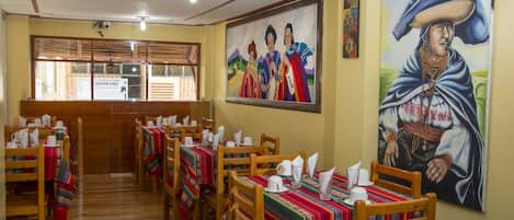 A restaurant with wooden tables and chairs, colorful tablecloths, and paintings on the walls.