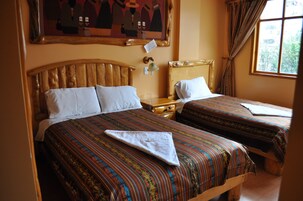 Habitación de hotel con dos camas, cada una con cabecero de madera y ropa de cama a rayas. Hay una mesita de noche con una lámpara entre las camas, y una ventana con cortinas a la derecha.