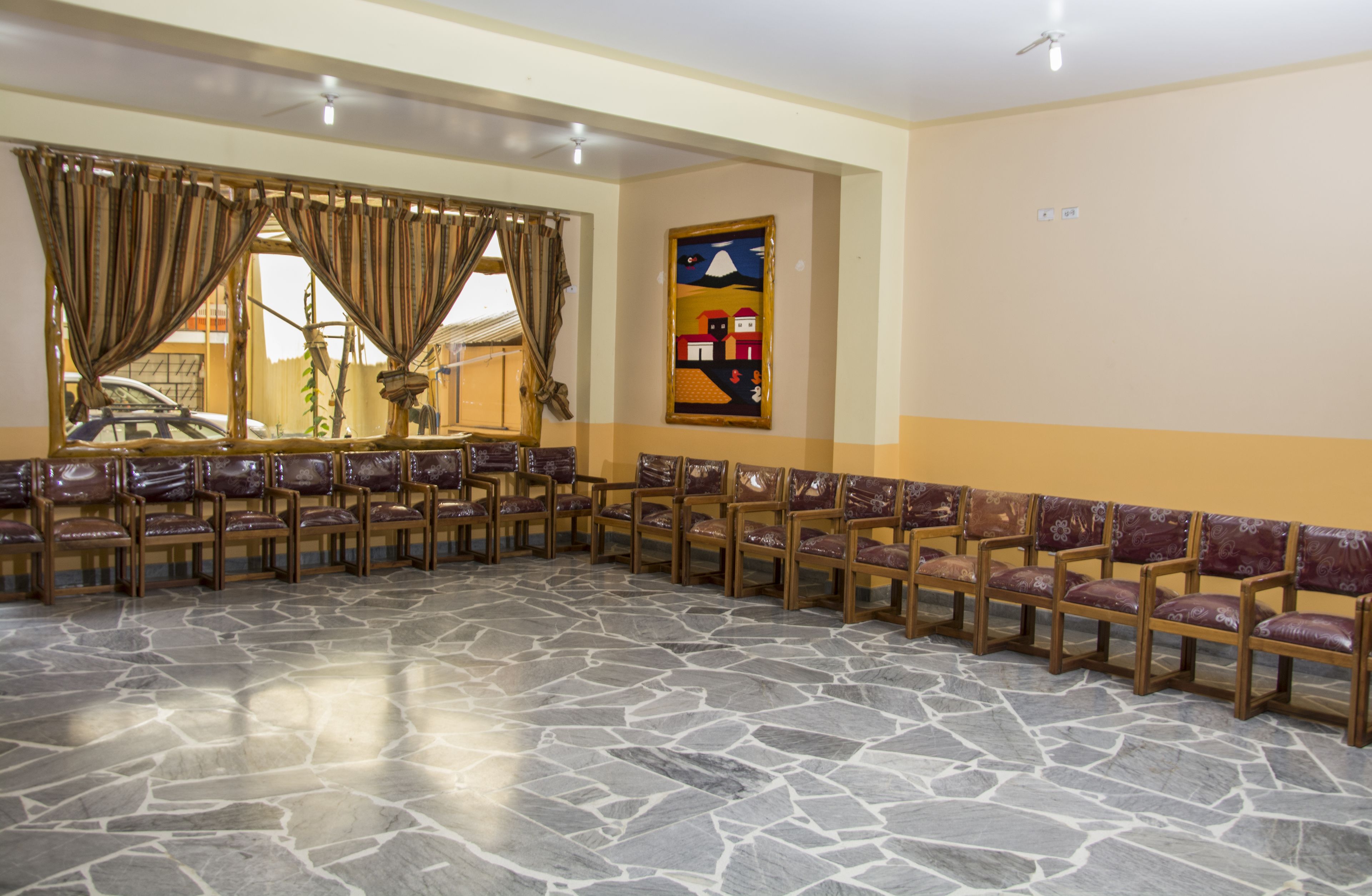 A conference room with a stone floor, wooden chairs, and a large window with curtains.