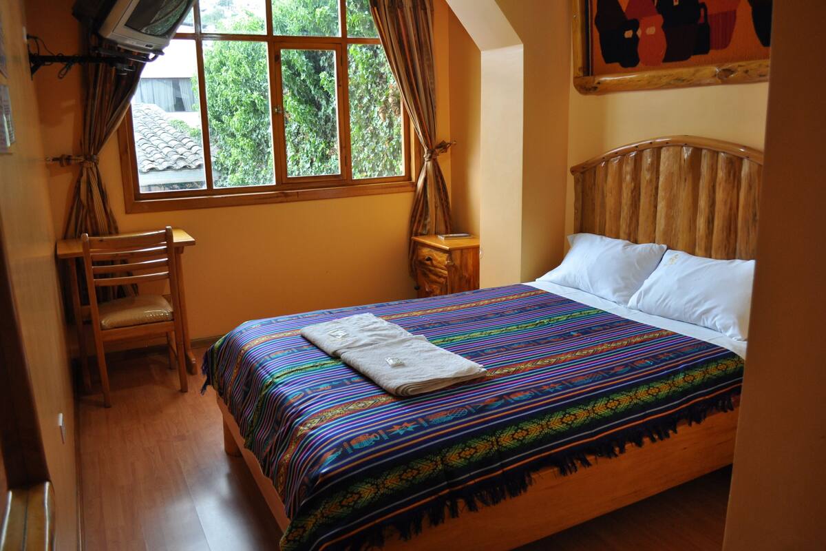 A bedroom with a wooden bed, a chair, a nightstand, and a window with curtains.