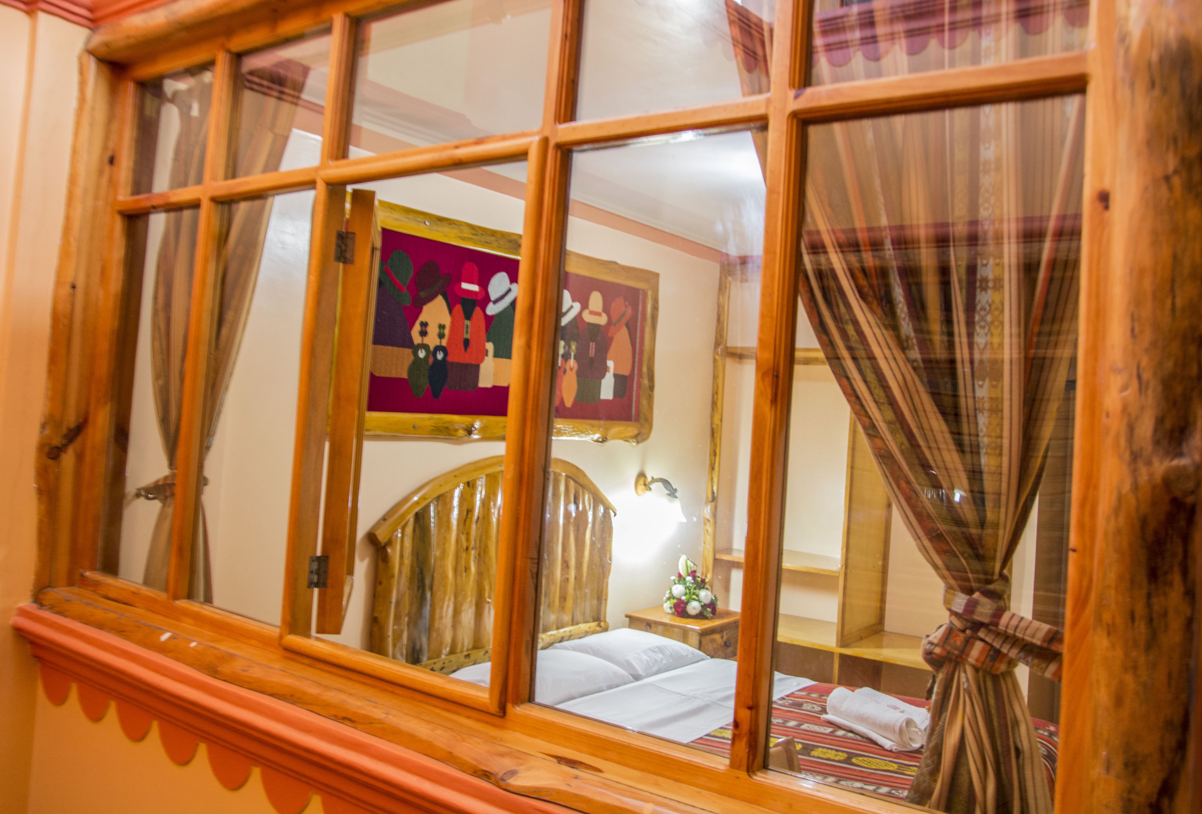 A room with a wooden headboard bed, a window with curtains, and a painting on the wall.