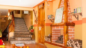 Una escalera con baldosas decorativas, una puerta de madera con un letrero, una pequeña mesa con libros, y una pared de ladrillo con chimenea y estanterías.