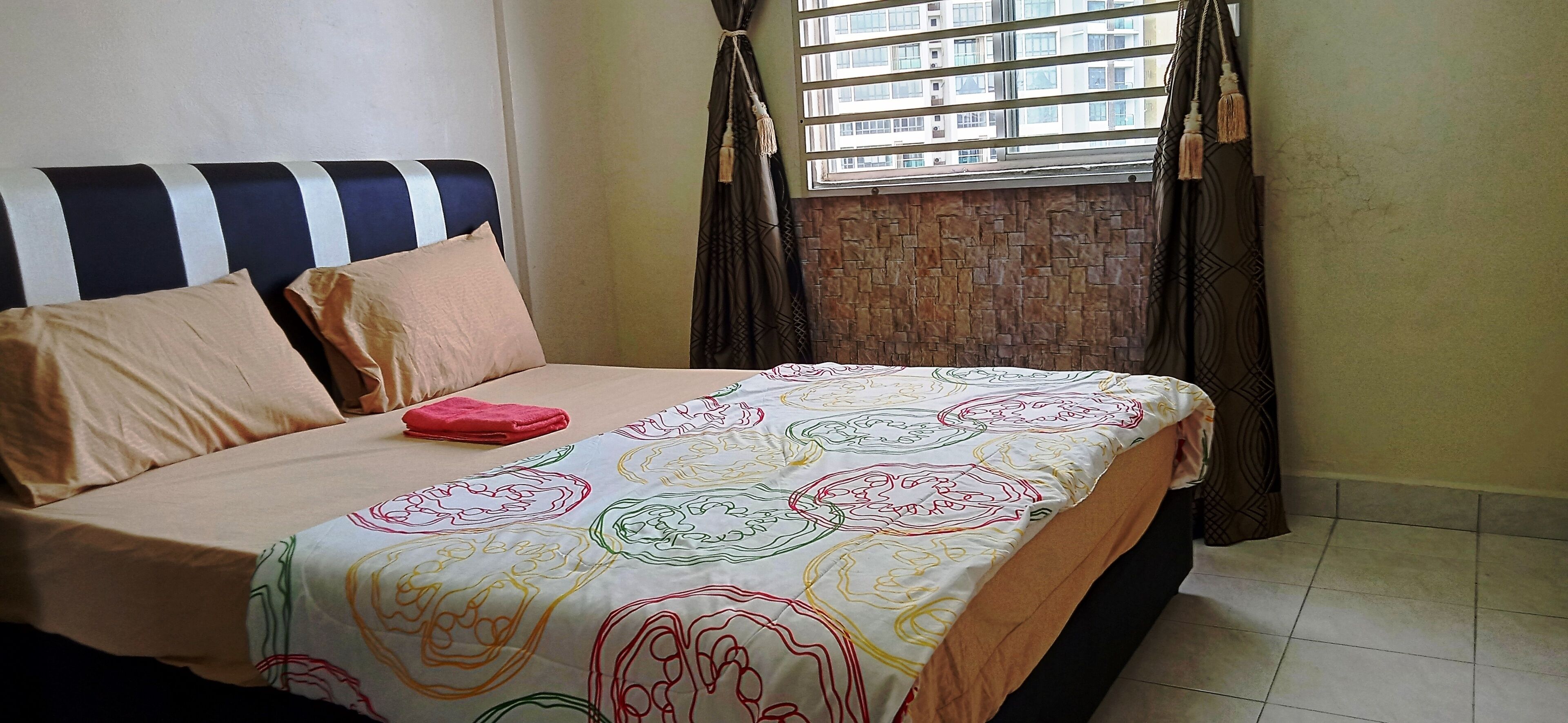Un lit avec une couvre-lit à motifs, une tête de lit à rayures et une fenêtre avec des rideaux.