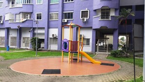 A playground with a slide and climbing structure in front of a multi-story building with balconies and windows. - Gateway Malaysia - Johor Bahru (Johor Bahru)