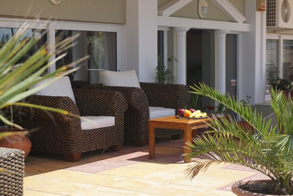 A patio area with two sofas, a small table with fruit, and potted plants. - Hotel Iraklis (Preveza)