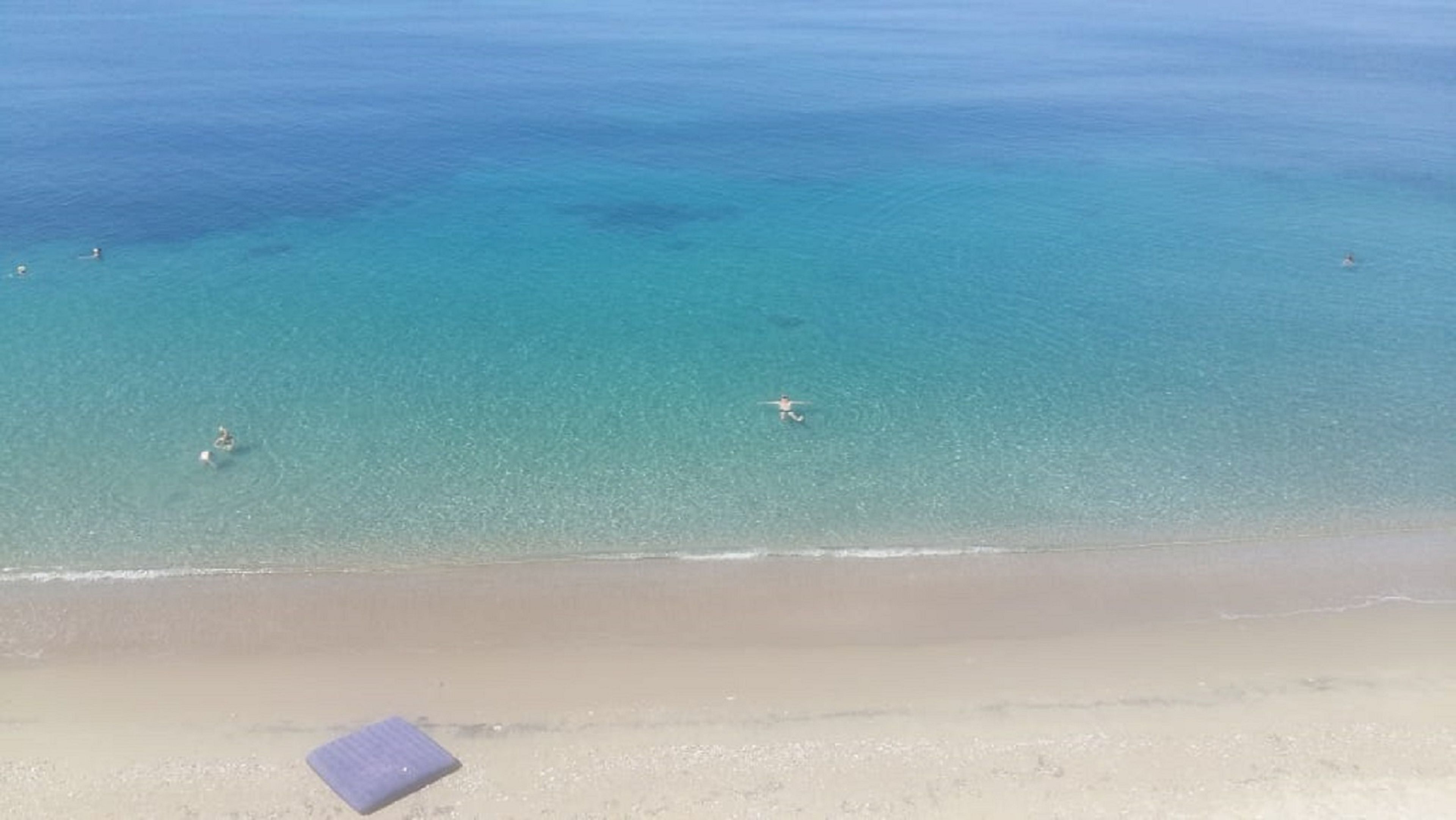 A beach with clear blue water and a sandy shore.