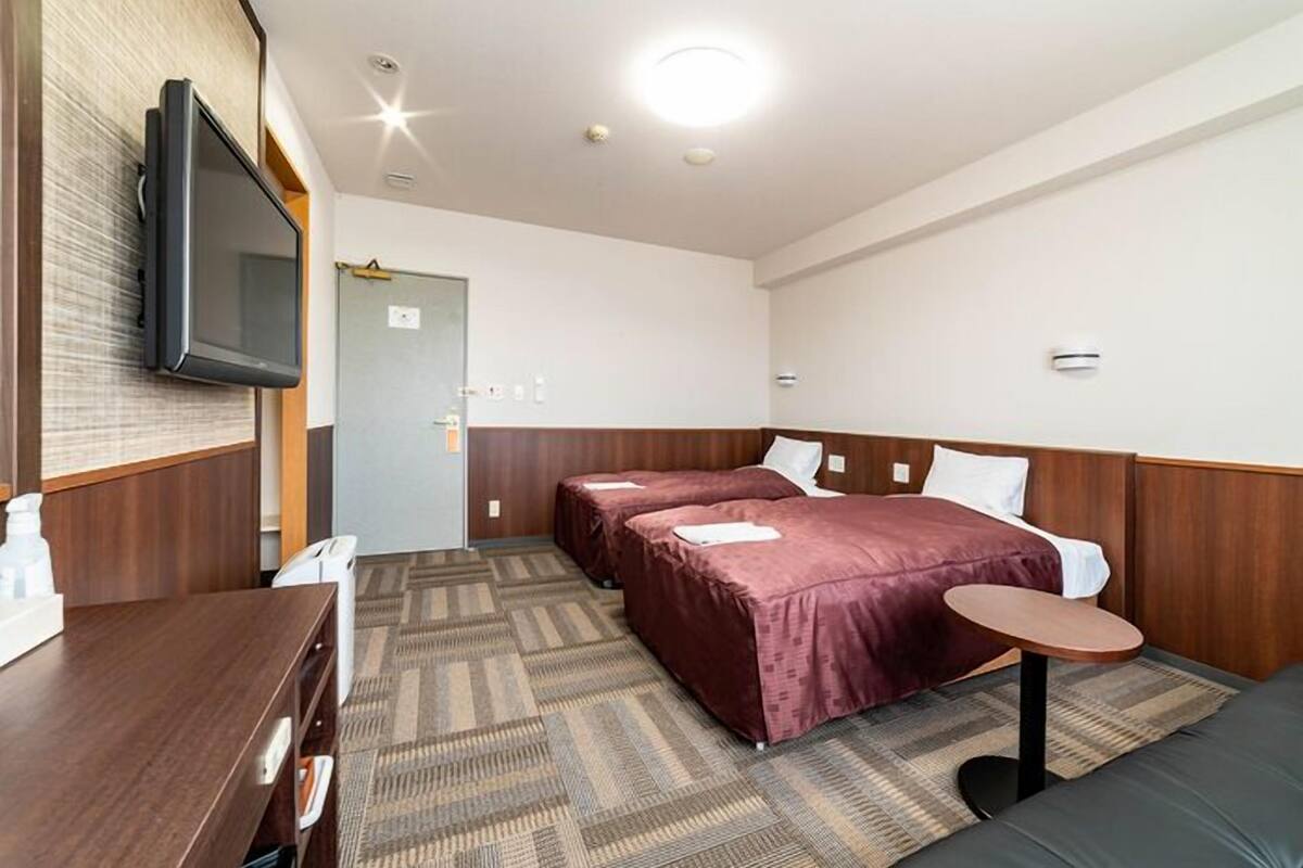 A hotel room with two beds, a TV, a desk, and a small table.