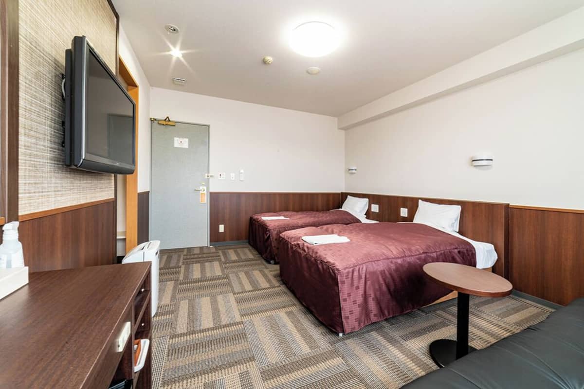 A hotel room with two beds, a TV, a desk, and a small table.