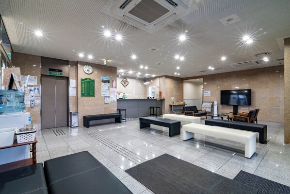 A modern lobby with seating areas, a reception desk, a clock, and a television.