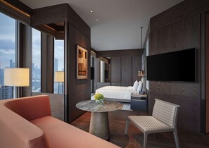 Une chambre d’hôtel moderne dotée d’un grand lit, d’un téléviseur fixé au mur, d’un coin salon avec une table et offrant une vue sur la ville grâce à de grandes fenêtres.