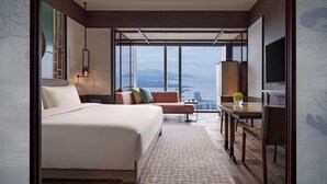 A modern hotel room with a large bed, a sofa, a dining table, and a TV. The room has large windows offering a city view. - Park Hyatt Shenzhen (Shenzhen)