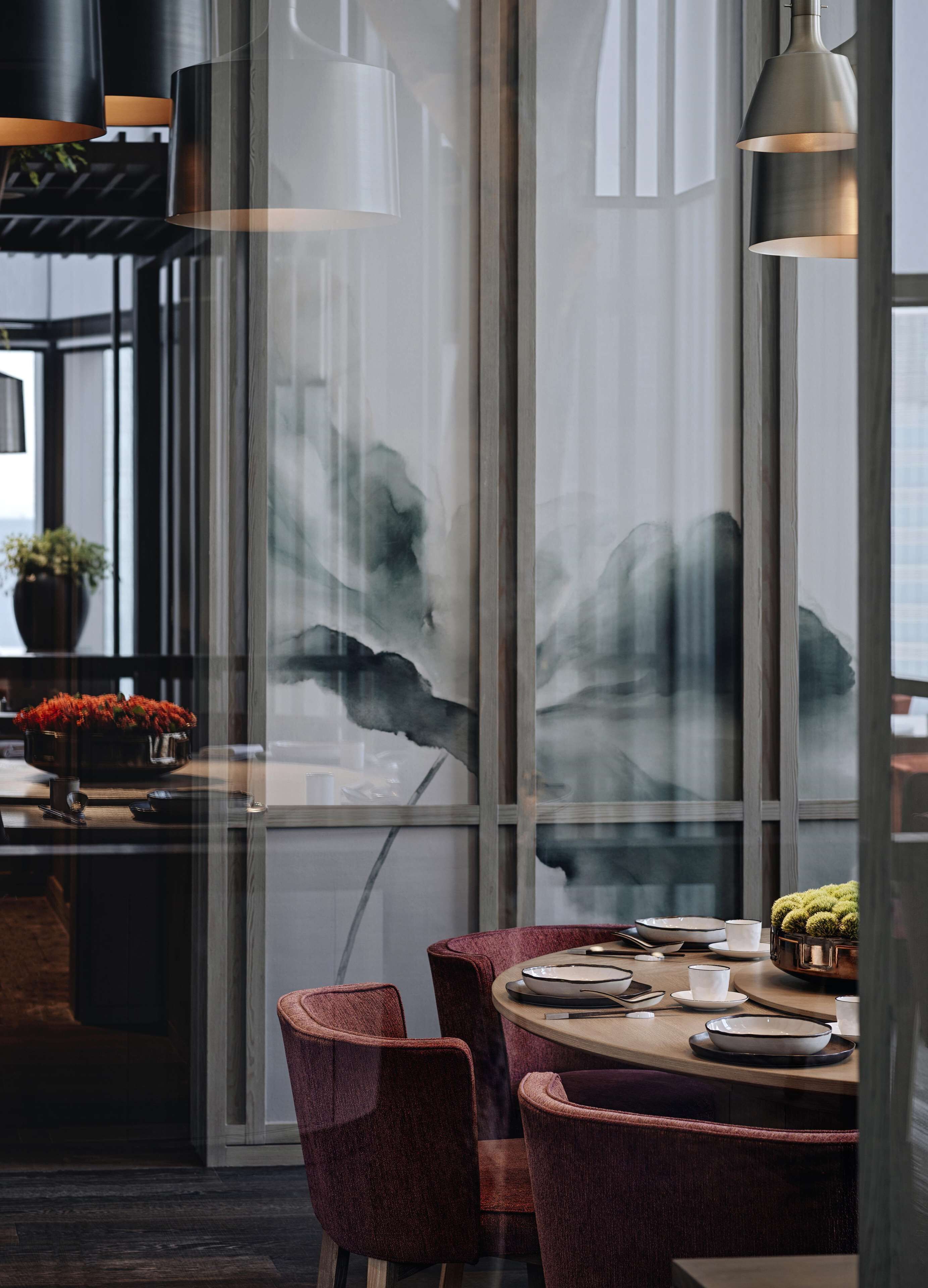 A modern dining area with a glass partition, red upholstered chairs, and a wooden table set with plates, bowls, and cups.