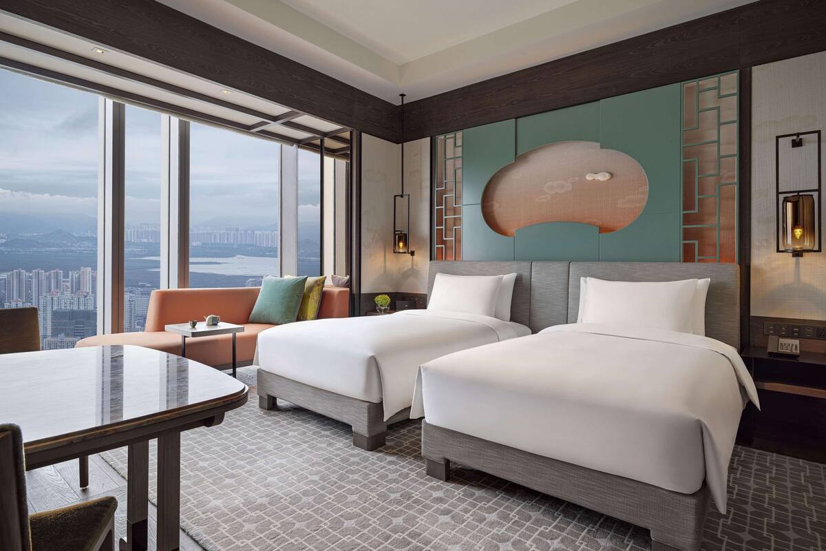 Habitación de hotel con dos camas, una mesa de comedor y vista a la ciudad.